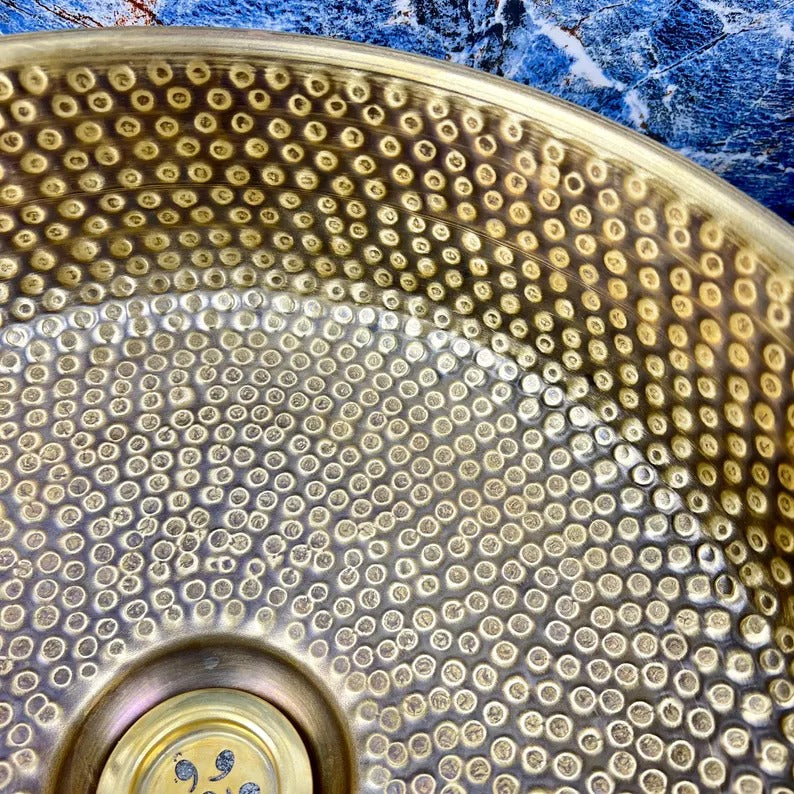 Close-up of hand-hammered brass round sink with unique dot pattern and drain, showcasing Moroccan artisan craftsmanship.