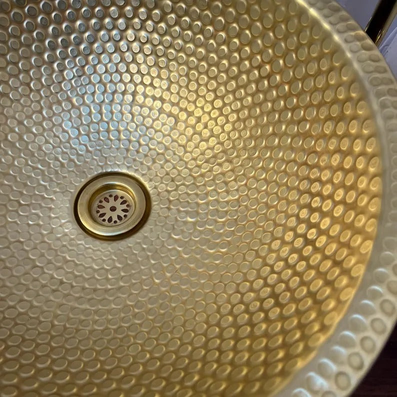 Close-up view of a handcrafted brass sink with a textured surface and drain hole.