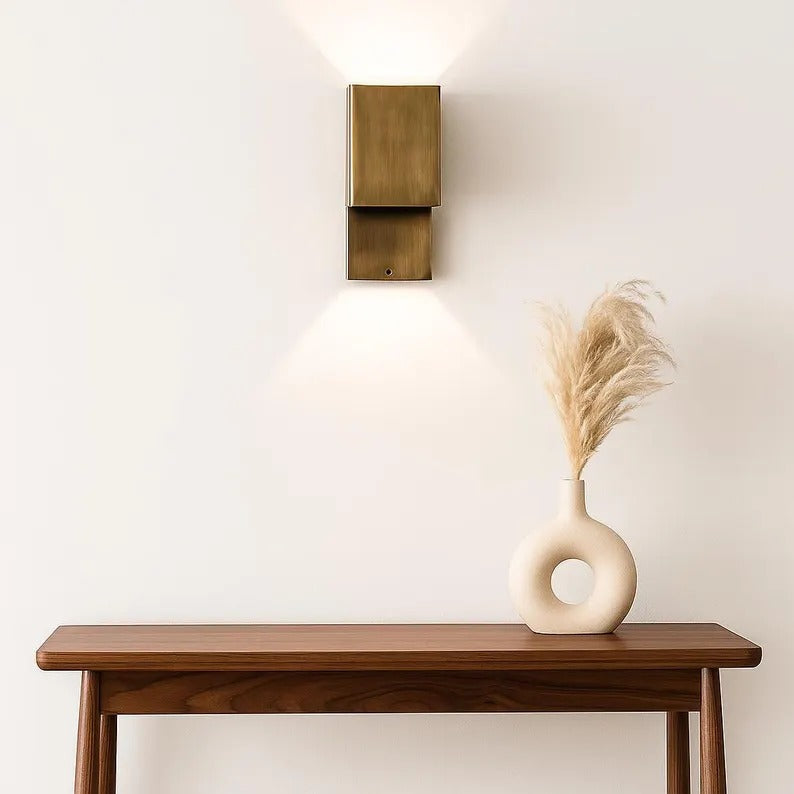 Handcrafted copper wall sconce with modern design, illuminating a stylish table with a vase and dried flowers.
