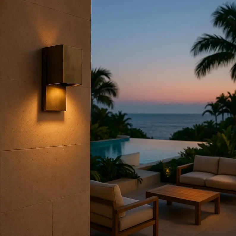 Modern brass wall sconce illuminating a patio area at sunset, highlighting minimalist design and warm ambiance.