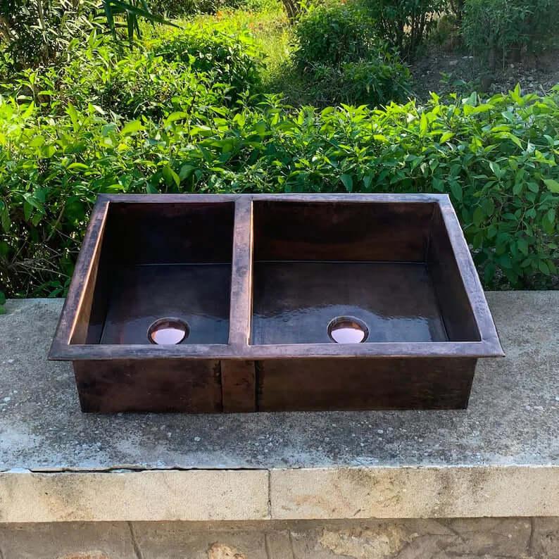 Handmade copper double vessel sink for kitchen, showcasing a rustic design with two basins on a natural stone surface.
