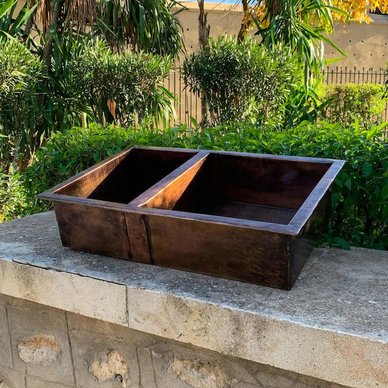 Cooper handmade double vessel sink for kitchen, showcasing elegant copper design in outdoor setting.