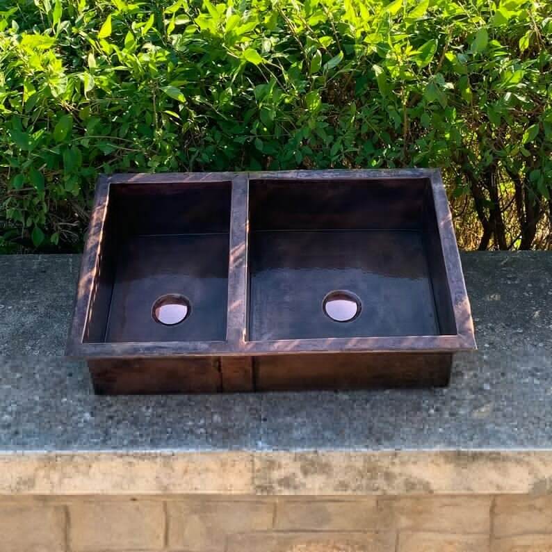 Cooper handmade double vessel sink for kitchen, featuring a copper design set against a green backdrop.