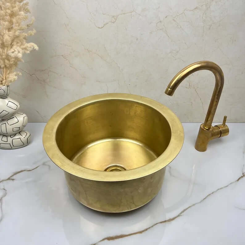 Handcrafted round brass basin sink with a stylish faucet, showcasing elegance for kitchen or bathroom use.