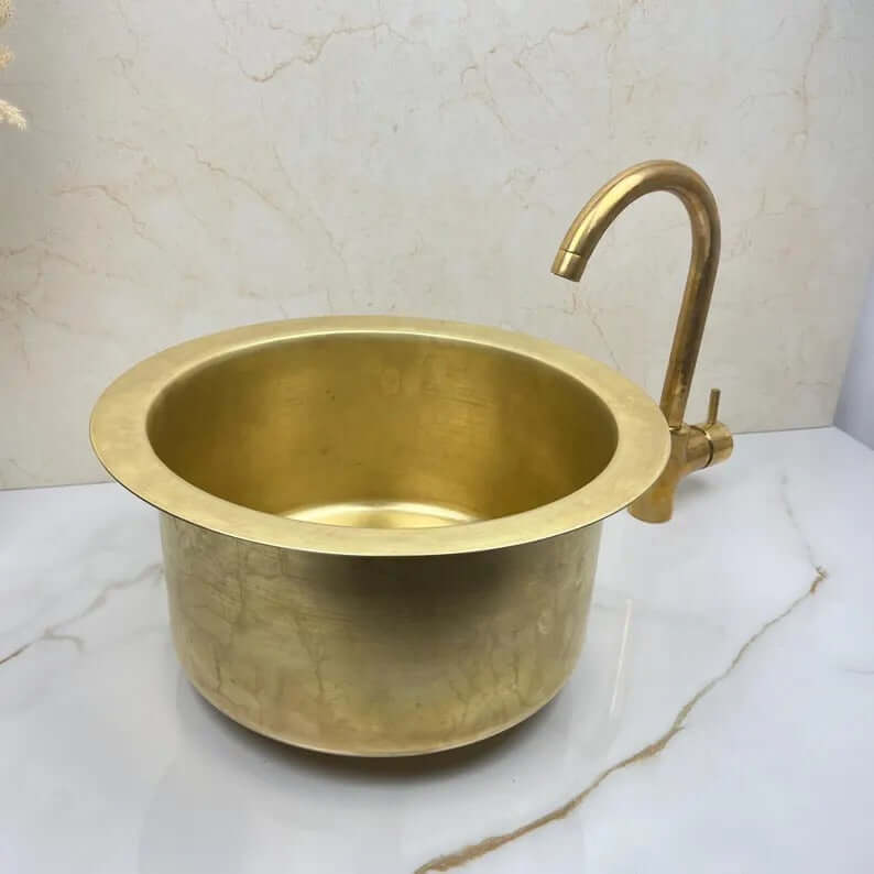Round brass basin sink with elegant curved faucet, handcrafted for kitchens and bathrooms.