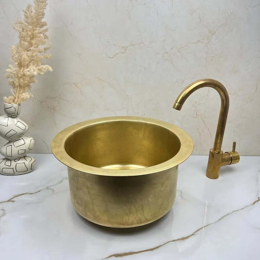 Handcrafted round brass basin sink with gold faucet, rustic and elegant for kitchen or bathroom.