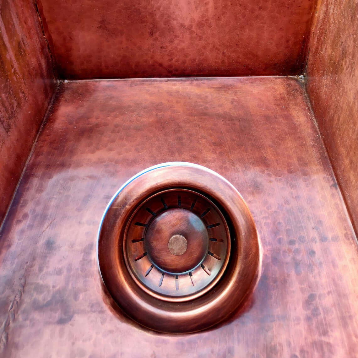 Interior view of a handmade double copper sink showcasing its hammered finish and drain design.