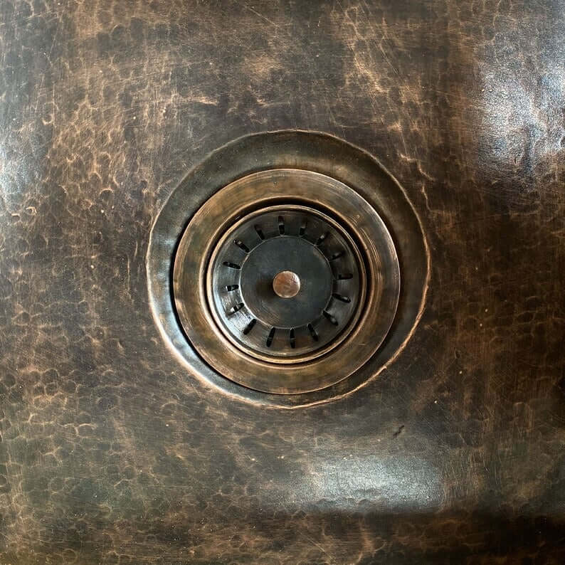 Close-up of a handmade copper sink drain, showcasing intricate texture and detail.