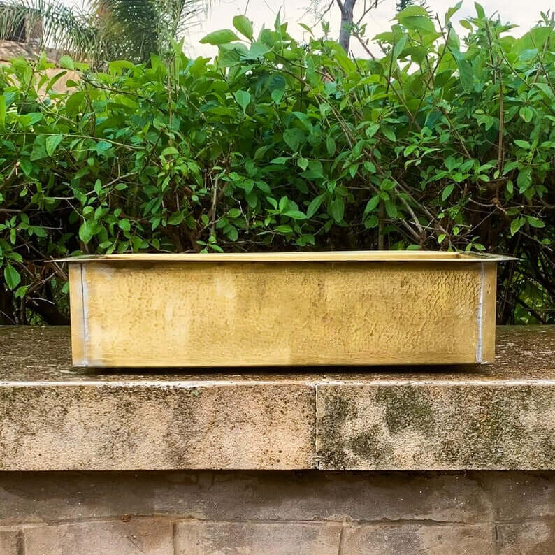 Handmade brass sink with a textured finish, showcasing artisanal Moroccan craftsmanship against greenery.