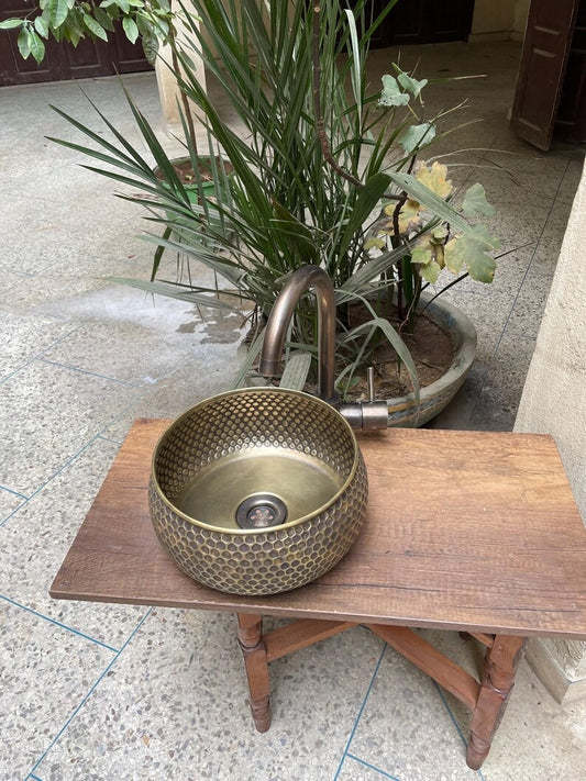 Hand hammered brass kitchen sink with intricate pattern on wooden table in a Moroccan setting.