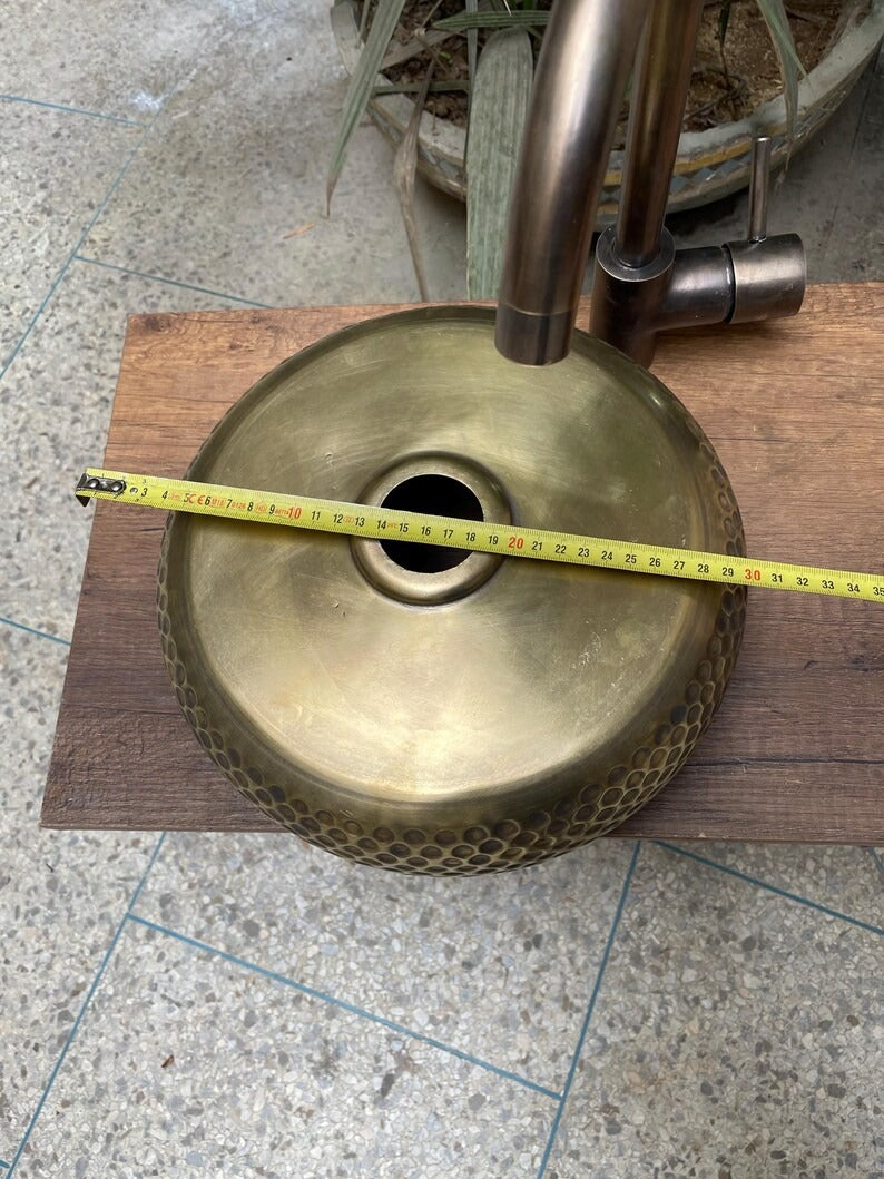 Hand hammered brass kitchen sink with measuring tape, showcasing Moroccan design elegance on a wooden surface.