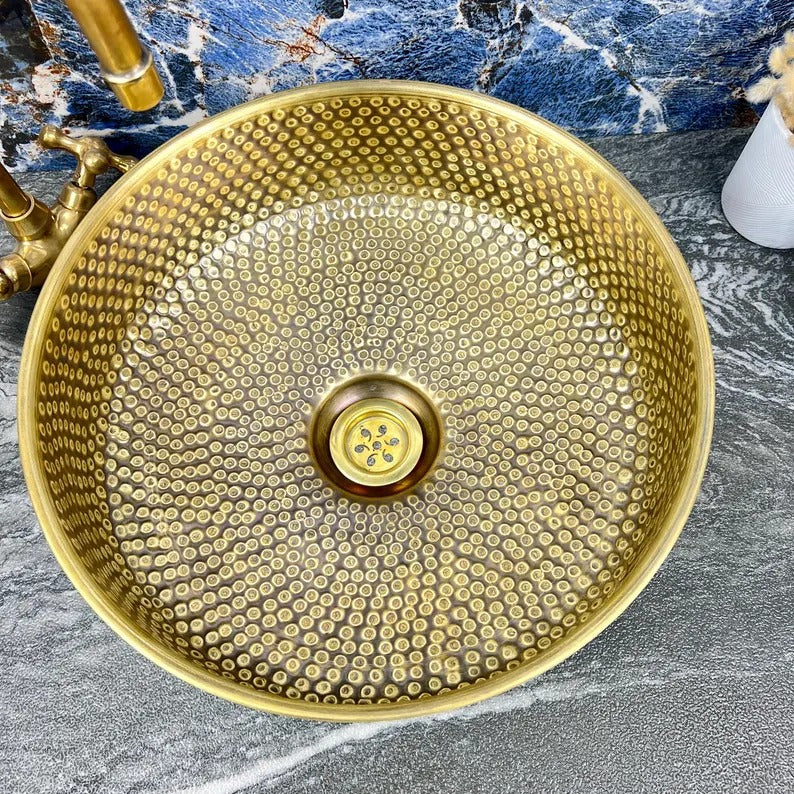 Hand-hammered brass round vessel sink featuring intricate detailing and a center drain, perfect for luxury bathrooms.