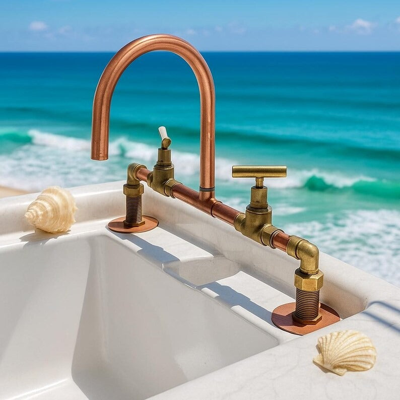 Handmade copper and brass faucet at an oceanfront sink, featuring rustic design and double handles.