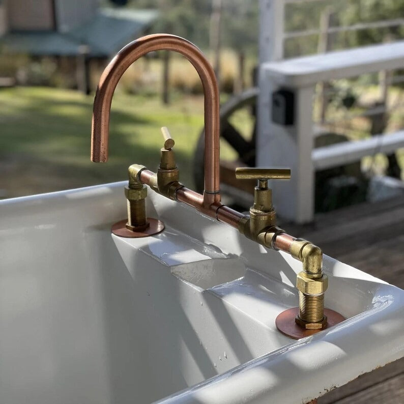 Handmade copper and brass faucet installed on a rustic sink, showcasing beautiful piping and double handles.