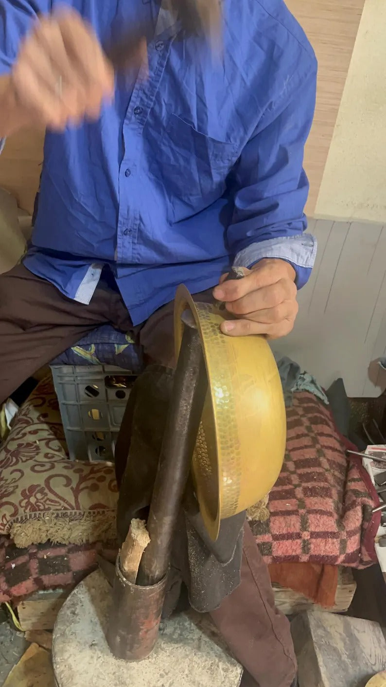 Artisan shaping a brass sink with a hammer in a workshop, showcasing traditional craftsmanship.