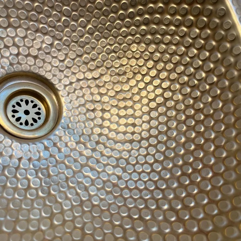 Close-up of a hammered brass sink basin featuring a unique pattern and drain hole.