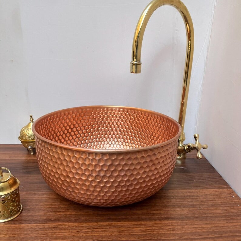 Brushed copper bathroom sink with a hammered design, paired with a gold faucet on a wooden countertop.