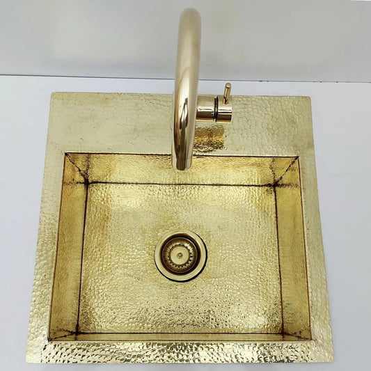 Unlacquered hammered solid brass sink with matching faucet and strainer, ideal for rustic or farmhouse kitchens.