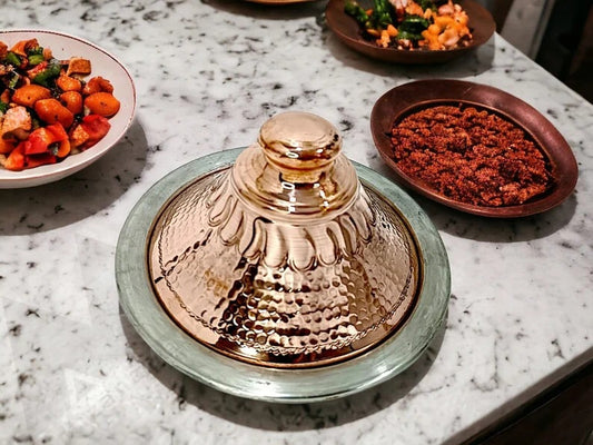 Handcrafted Moroccan copper tagine with lid on a marble table, surrounded by colorful dishes.