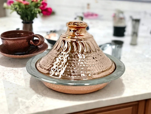 Luxurious handcrafted Moroccan copper tagine with lid and serving tray on kitchen counter, adorned with a floral pattern.