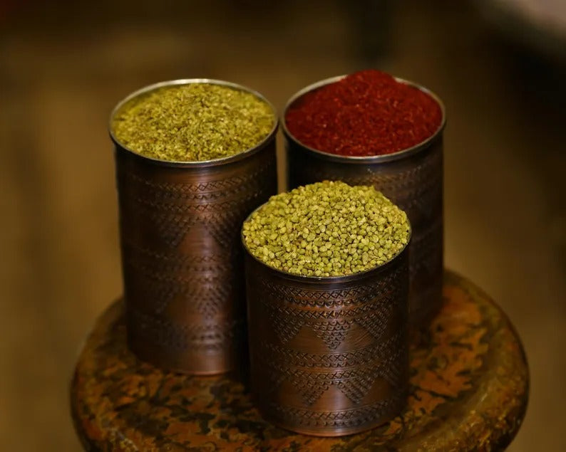 Set of three handmade copper spice containers filled with green and red spices, showcasing elegant kitchen decor.