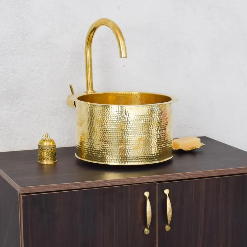 Brass handmade Moroccan sink with a sleek design on a wooden cabinet, featuring a stylish faucet and decorative items.