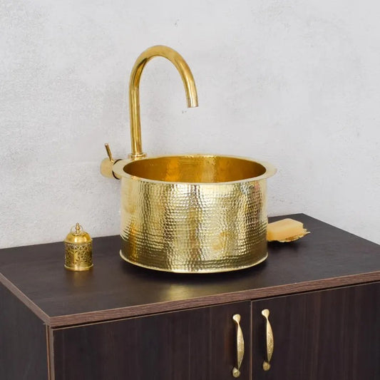 Handmade brass sink with modern faucet and decorative gold elements on wooden cabinet