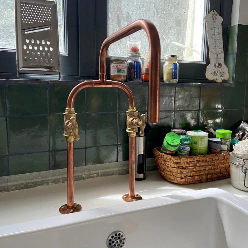 Handmade pure copper deck mount faucet with brass valves and U-shaped spout in a rustic kitchen setting.